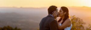 Engagement photo of couple kissing in front of a sunset in the mountains